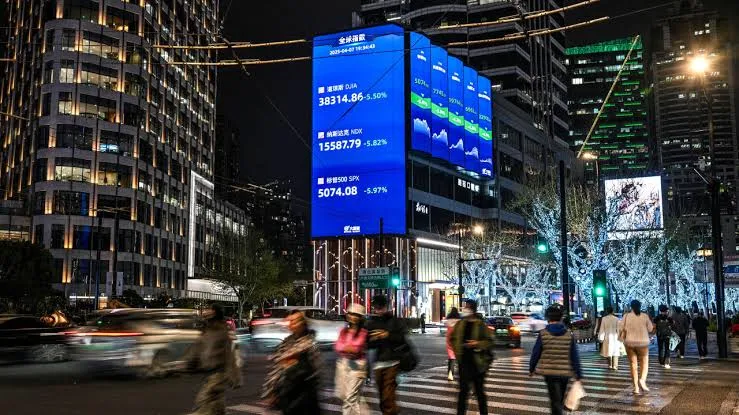 People walk past a large stock market display in a Chinese city at night.