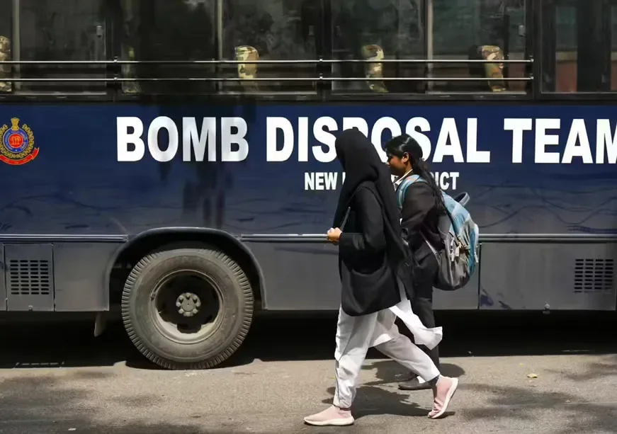A bomb disposal team bus with school students walking past after bomb threats to Delhi schools